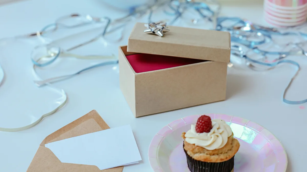 Birthday gift card table idea with an open gift box, blank card, envelope, cupcake, balloons, and party decorations.